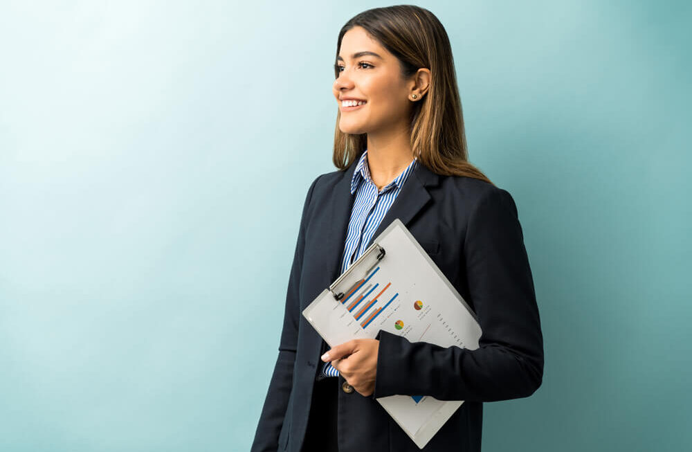 Agência Simi empresaria-atraente-segurando-area-de-transferencia-com-grafico-enquanto-desvia-o-olhar-contra-o-fundo-colorido