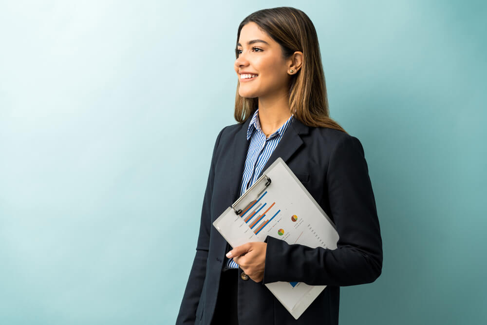Agência Simi empresaria-atraente-segurando-area-de-transferencia-com-grafico-enquanto-desvia-o-olhar-contra-o-fundo-colorido