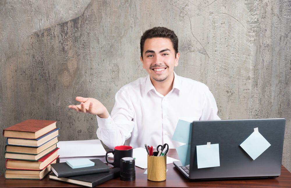 Agência Simi jovem-empresario-feliz-olhando-para-camera-na-mesa-escritorio