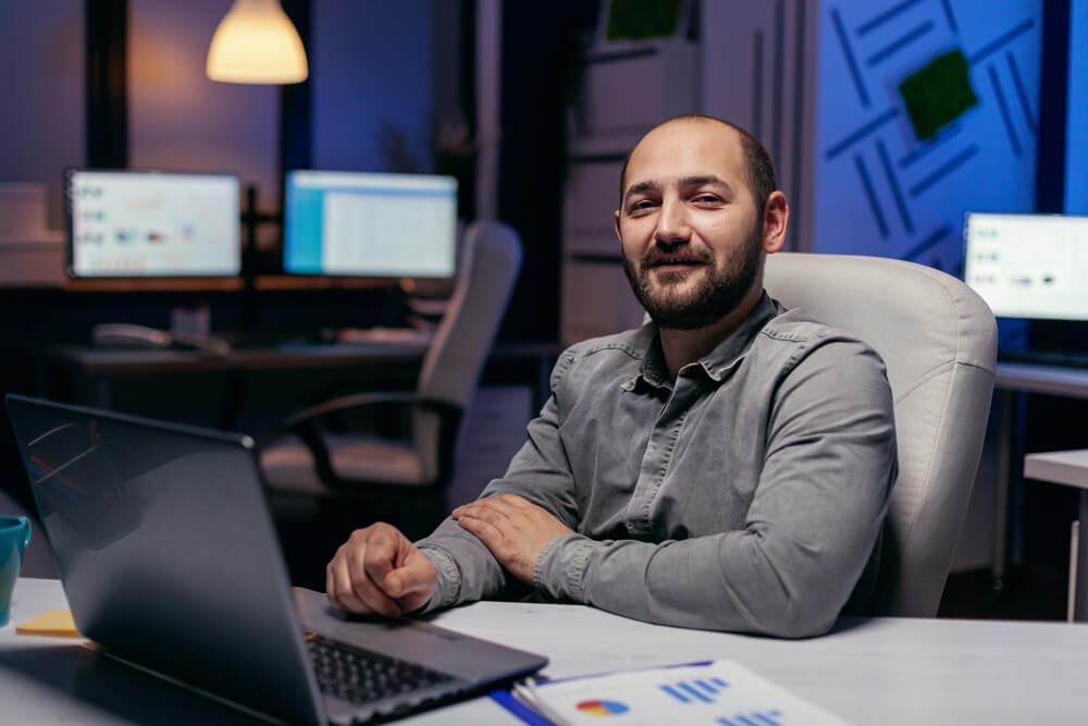 Agência Simi retrato-de-freelancer-olhando-para-camera-sentado-na-mesa-com-graficos-homem-de-negocios-inteligente-sentado-em-seu-local-de-trabalho-durante-as-primeiras-horas-da-noite-fazendo-s